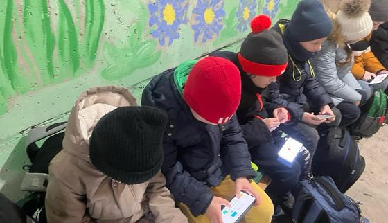 Amidst the threat of drone attacks, children find a moment of learning with 'Can't Wait to Learn' app on their gadgets in a shelter.