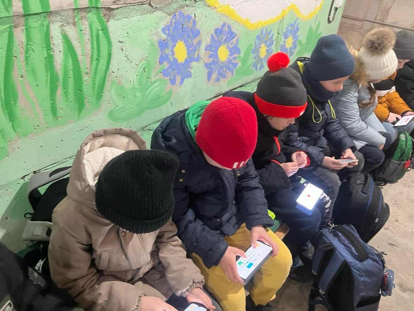 Amidst the threat of drone attacks, children find a moment of learning with 'Can't Wait to Learn' app on their gadgets in a shelter.