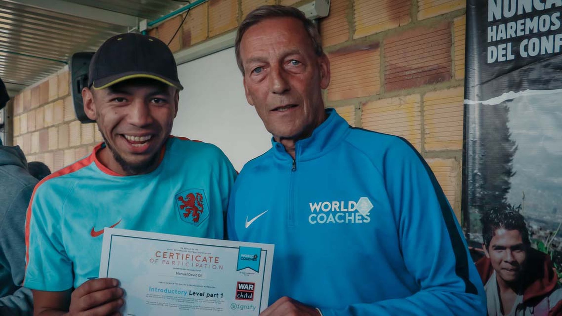War Child Colombia Play it For Life participant Manuel with diploma, standing alongside Johan Neeskens